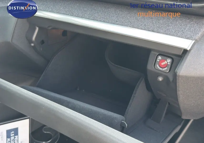 Intérieur du Peugeot 5008 2023 montrant la boîte à gants ouverte avec revêtement noir et détails de commande airbag.