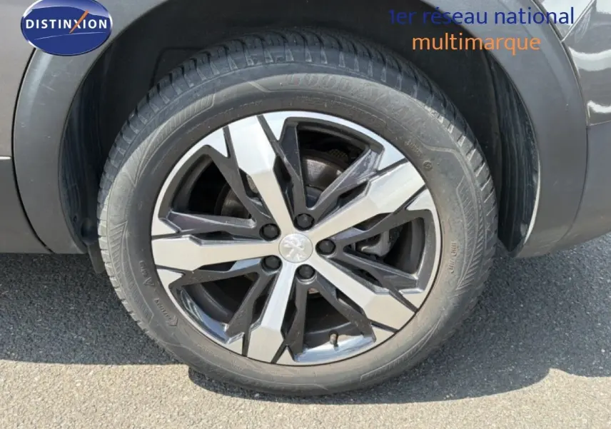 Gros plan sur la roue avant droite du Peugeot 5008 gris Platinium avec jante alliage bicolore et logo lion central.