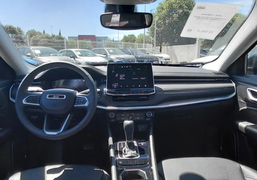 Vue intérieure avant du Jeep Compass 2025 bleu, montrant le volant, écran tactile central et levier de boîte automatique.