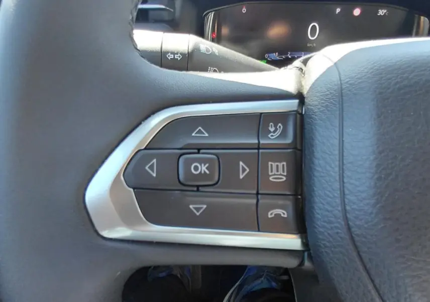 Gros plan sur les commandes gauche du volant du Jeep Compass 2025, montrant les boutons multifonctions noirs et argentés.