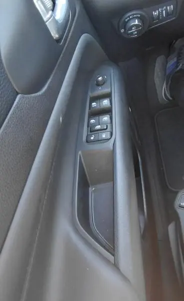 Vue rapprochée du panneau de porte côté conducteur du Jeep Compass bleu 2025, avec commandes électriques et réglage des phares.