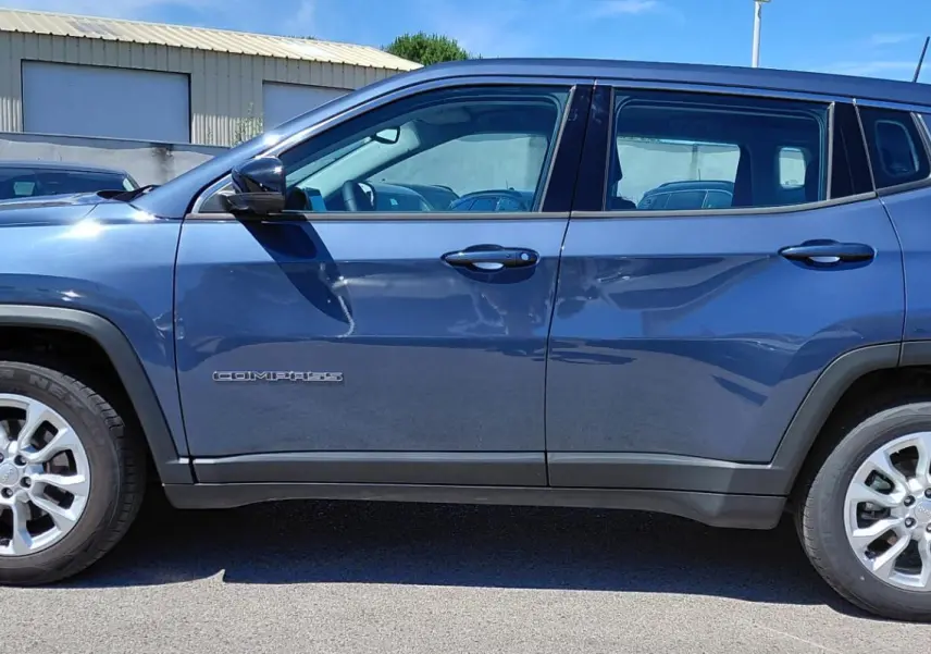 Vue de profil côté gauche d'un Jeep Compass bleu 2025 avec jantes alliage 18 pouces et logo visible sur la porte.