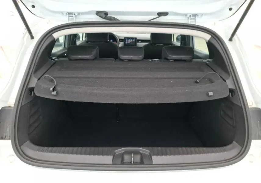 Vue arrière du coffre ouvert d'une Renault Clio blanche 2024 avec plage arrière noire et sièges arrière visibles.