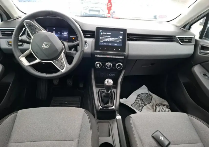 Vue intérieure avant de la Renault Clio blanche 2024, avec tableau de bord moderne et boîte manuelle.