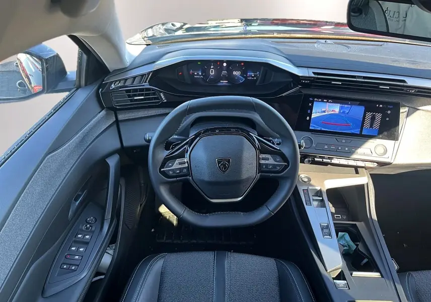 Vue intérieure de face du poste de conduite de la Peugeot 308 noire, avec volant compact et écran tactile affichant la caméra de recul.