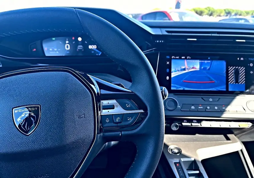 Vue intérieure centrée sur le volant Peugeot noir et l'écran tactile affichant la caméra de recul de la 308 1.5 BlueHDi 2025.