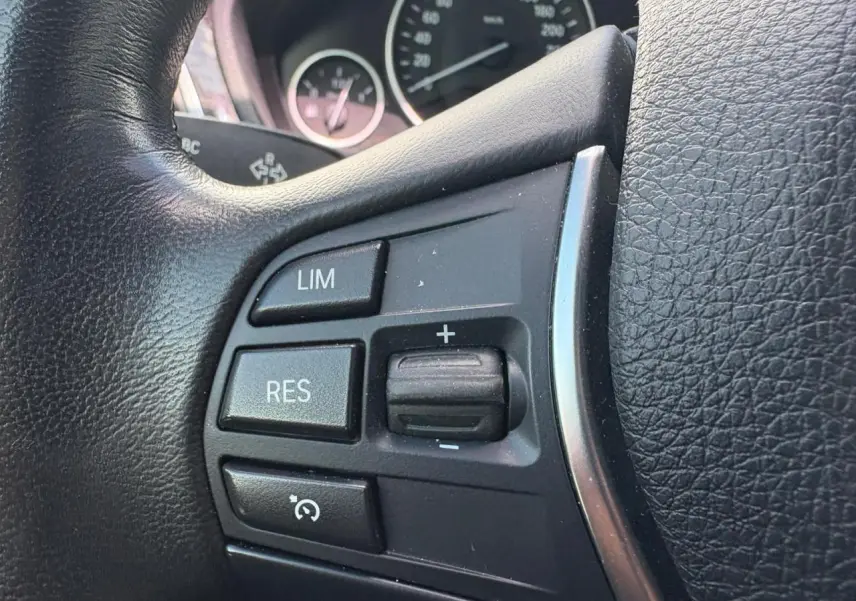 Gros plan sur les commandes du régulateur de vitesse au volant cuir noir d'une BMW Série 4 Gran Coupé 420d.