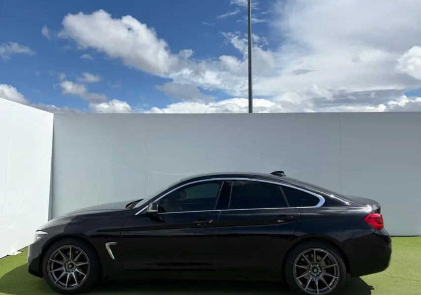 BMW Série 4 Gran Coupé noir saphir vue de profil côté gauche, avec jantes alliage 18 pouces et toit ouvrant.