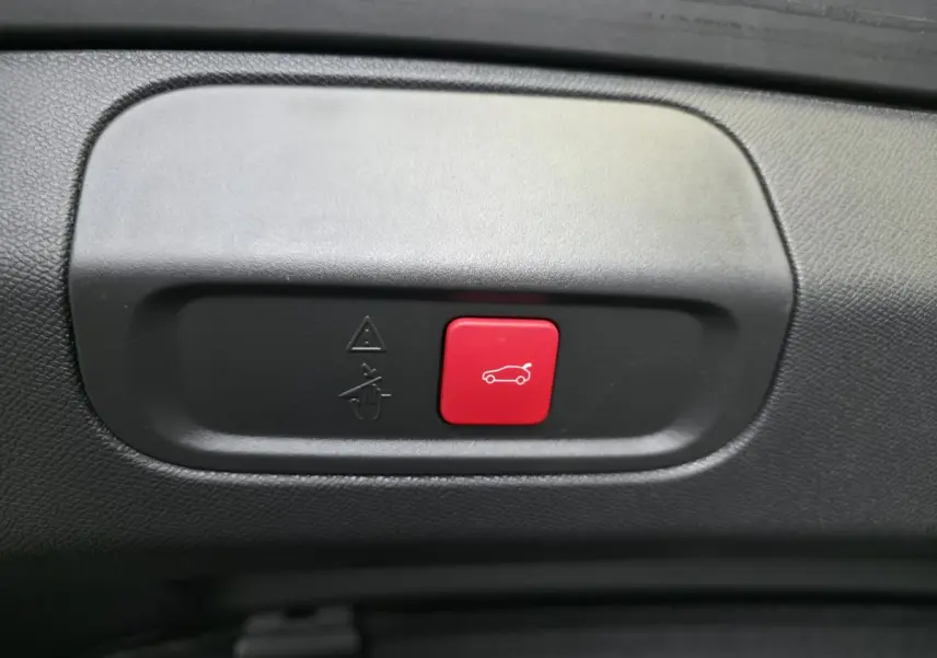 Bouton rouge d'ouverture électrique du hayon sur panneau intérieur noir d'une Peugeot 408 gris 2024 Berline GT hybride rechargeable