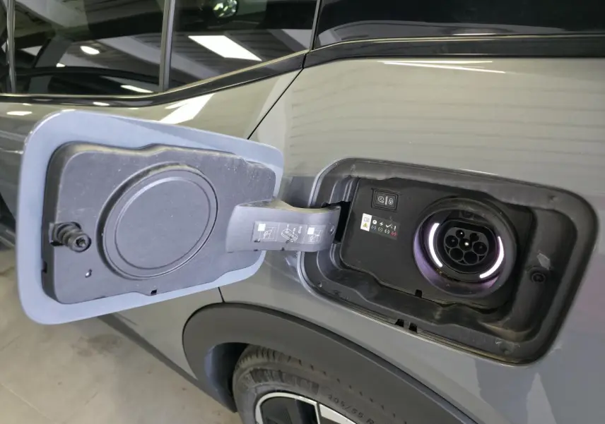 Prise de recharge ouverte côté gauche sur la carrosserie gris métallisé d'une Peugeot 408 hybride rechargeable 2024.