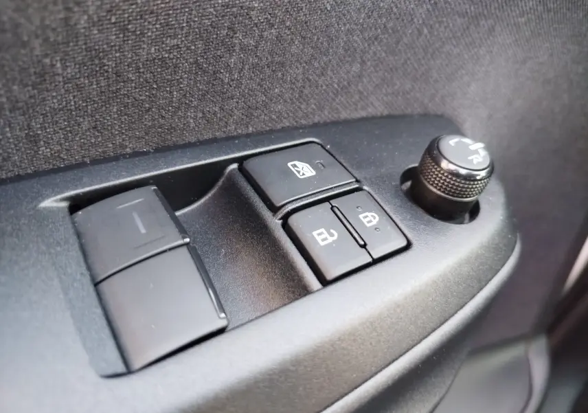 Gros plan sur les commandes de lève-vitres et réglage des rétroviseurs côté conducteur d'une Toyota Yaris blanche.