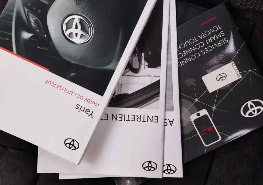 Image montrant plusieurs manuels d'utilisation Toyota Yaris 2023, posés en éventail sur un siège, avec logo Toyota visible.