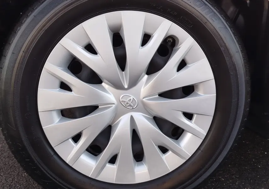 Gros plan sur la roue avant droite d'une Toyota Yaris blanche avec enjoliveur argenté au design dynamique.