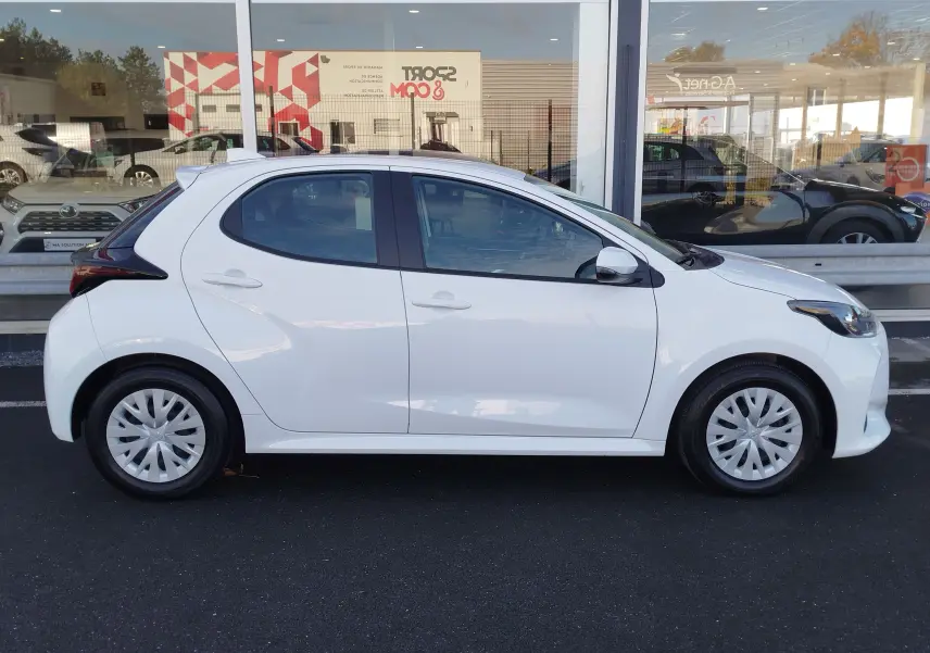 Profil côté gauche d'une Toyota Yaris blanche 5 portes, version Dynamic Business 2023, garée devant une vitrine.