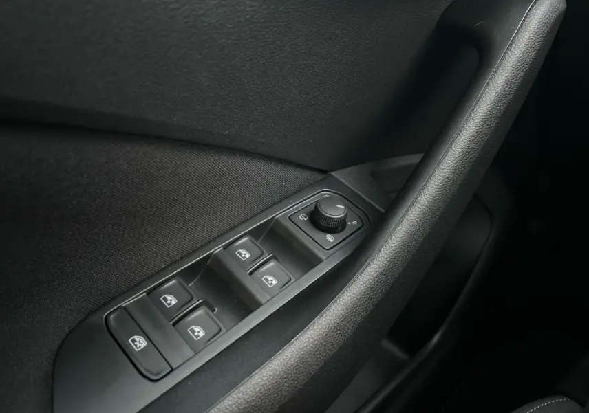 Gros plan sur les commandes de lève-vitres et rétroviseurs noirs à l'intérieur côté conducteur du Skoda Kamiq gris clair 2025.