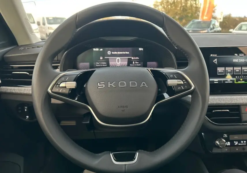 Vue rapprochée du volant cuir noir marqué SKODA et du tableau de bord numérique du SUV KAMIQ gris clair 2025.