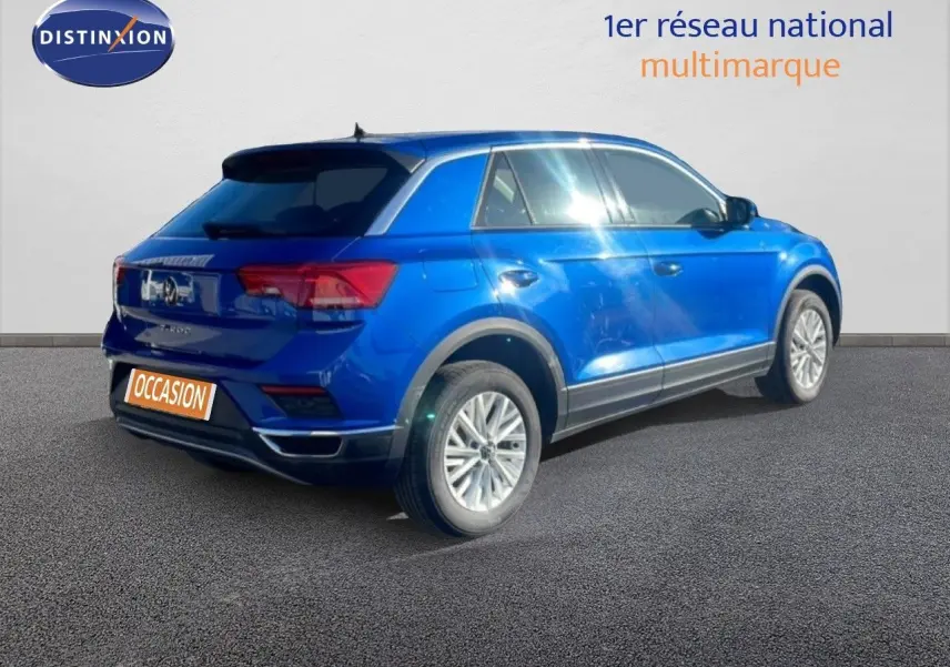 Vue 3/4 arrière droite d'un Volkswagen T-Roc bleu Ravenna métallisé sur fond neutre, avec jantes alliage et feux LED.