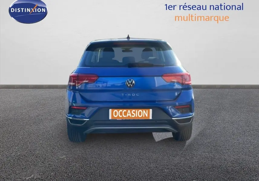 Vue arrière d'un Volkswagen T-Roc bleu Ravenna métallisé avec plaque occasion sur un sol goudronné.