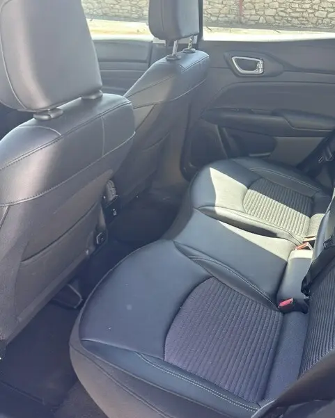 Vue intérieure arrière droite du Jeep Compass 2025 noir, montrant les sièges en cuir et tissu avec accoudoir central.