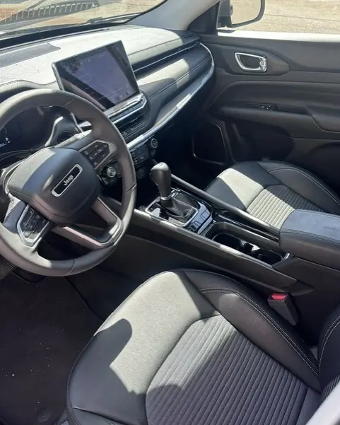 Vue intérieure côté conducteur du Jeep Compass 2025 noir, avec écran tactile, volant multifonction et accoudoir central.