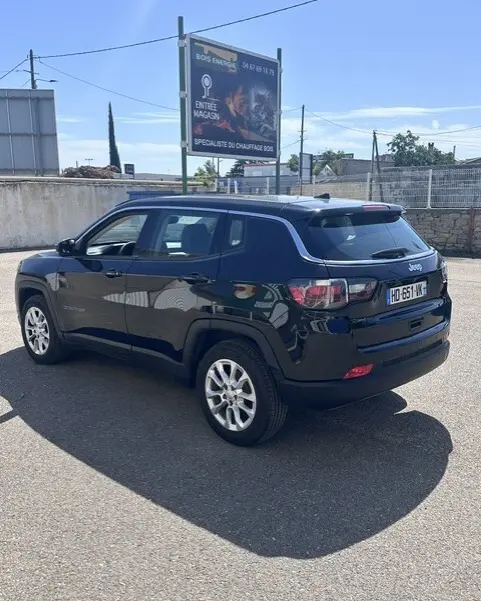 Jeep Compass noir vue 3/4 arrière droit, jantes alliage 18 pouces, toit noir avec barres de toit, stationné en extérieur.