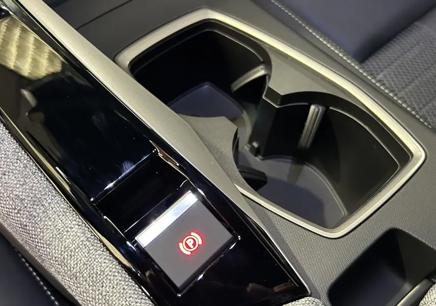 Gros plan sur la console centrale noire brillante avec bouton frein à main électronique et porte-gobelets du Peugeot 5008 gris Artense.