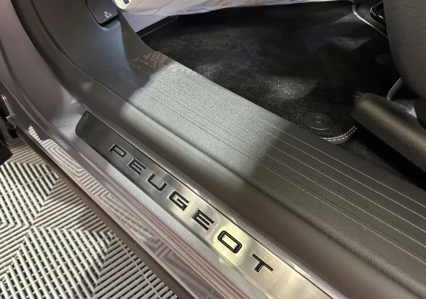 Gros plan sur la plaque de seuil de porte Peugeot en métal brossé à l'entrée côté conducteur, intérieur noir.