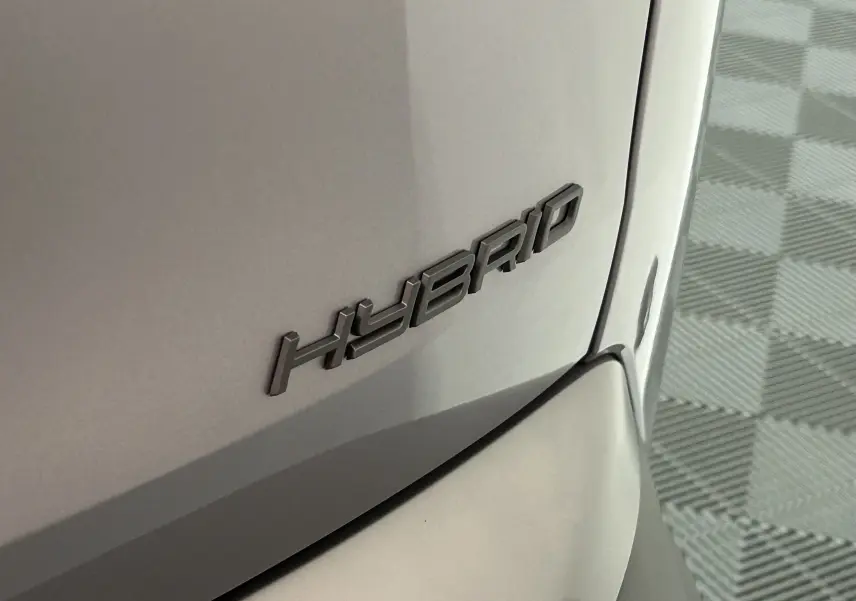 Gros plan sur l’inscription HYBRID en relief sur la carrosserie gris Artense d’un Peugeot 5008 III GT hybride.