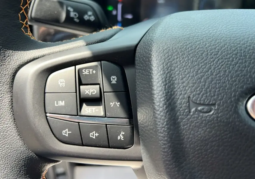 Gros plan sur les commandes à gauche du volant noir du Ford Ranger 2.3 PHEV Wildtrak Plus 2025, avec surpiqûres marron.