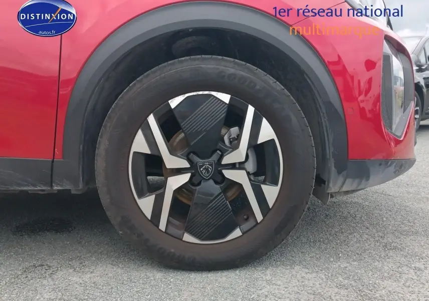 Gros plan sur la roue avant droite d’un Peugeot 2008 rouge elixir avec jante alu au design moderne.