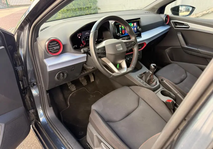 Intérieur côté conducteur de la SEAT Ibiza 2025 gris foncé, volant multifonction et détails rouges autour des aérateurs.