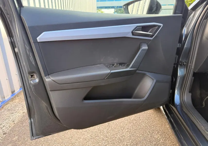Vue intérieure de la porte avant gauche d’une SEAT Ibiza 1.0 TSI 95 FR gris foncé avec garniture noire et insert argenté.