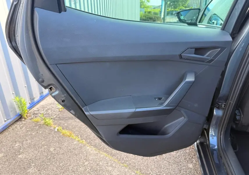 Vue intérieure sur la porte arrière gauche ouverte d'une SEAT Ibiza 2025 gris foncé, avec poignée et commande de vitre.