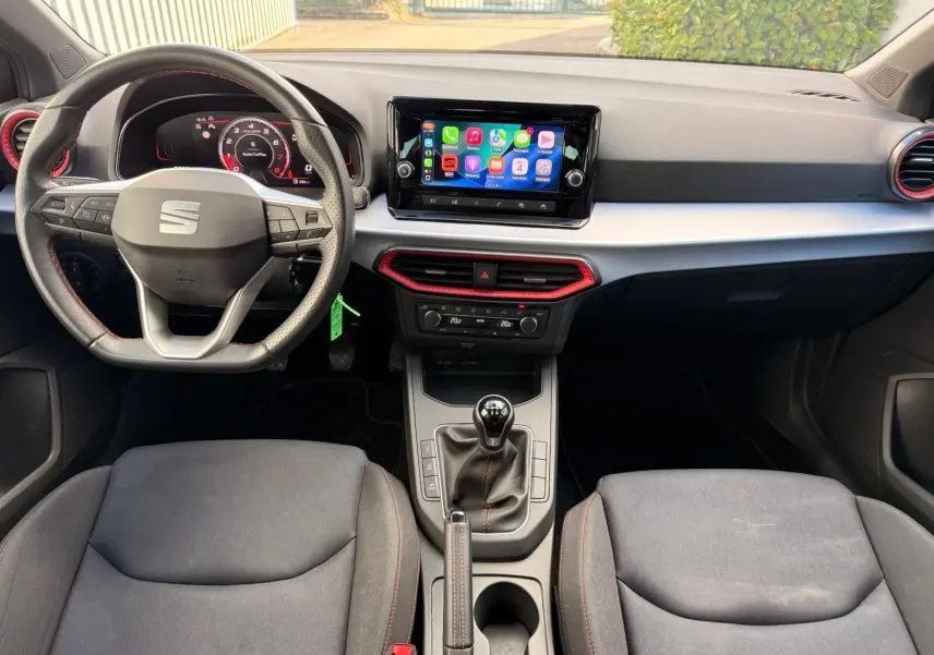 Vue intérieure avant de la SEAT Ibiza 1.0 TSI 95 FR 2025, tableau de bord avec écran tactile et volant sport noir avec surpiqûres rouges.