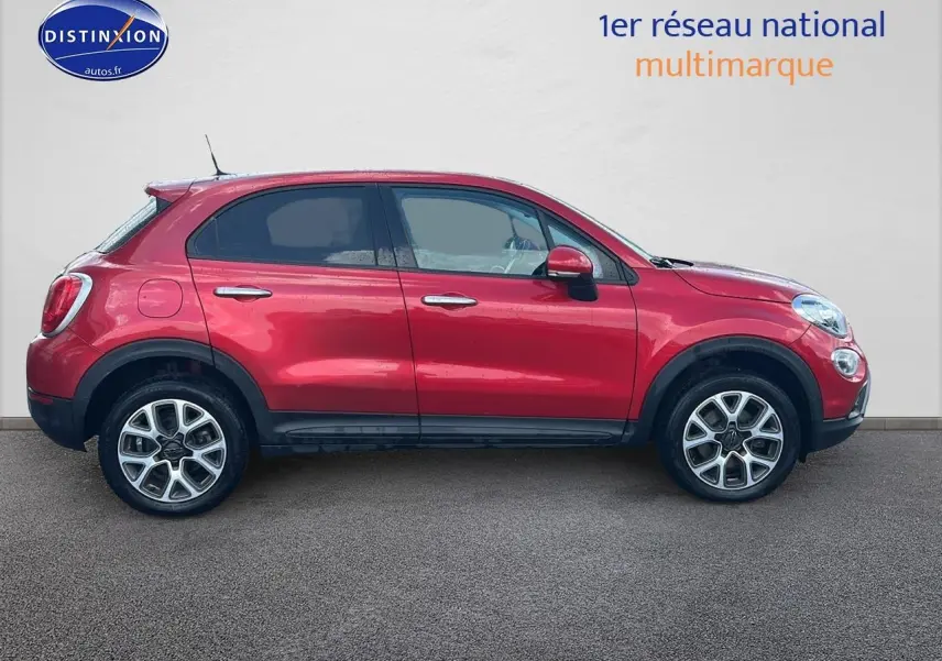 Profil droit d'un FIAT 500X rouge 2016 avec jantes alu et barres de toit, garé devant un mur clair.