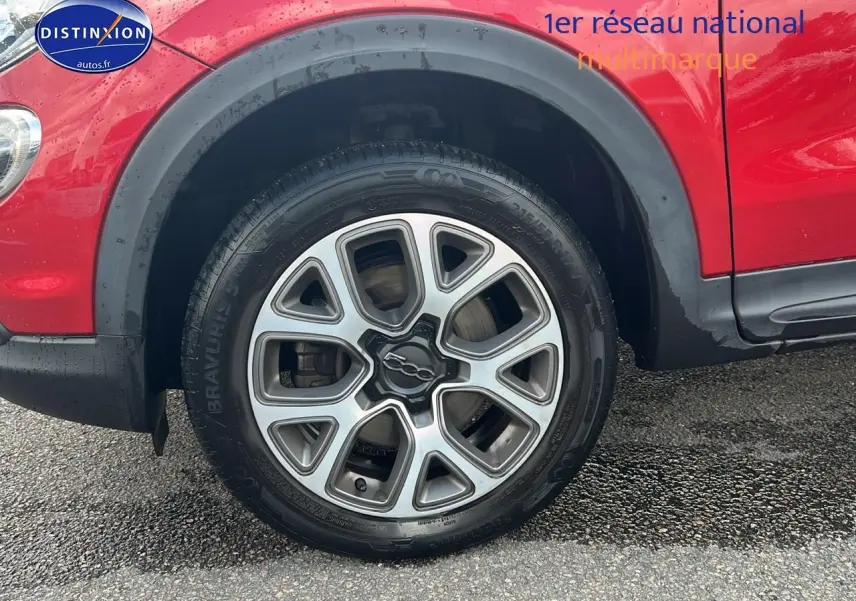 Gros plan sur la roue avant gauche rouge d'une Fiat 500X 2016 avec jante alu et entourage noir.