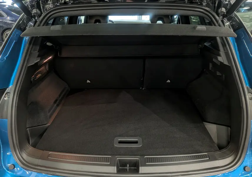 Coffre ouvert vu de l'arrière d'un Renault Austral bleu outremer avec toit noir, intérieur spacieux et tapis noir.