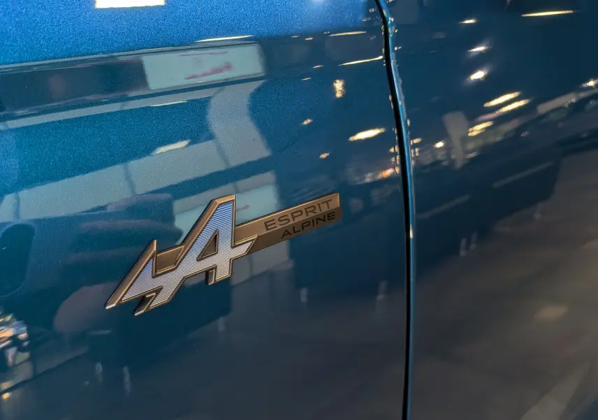 Gros plan sur l'écusson Esprit Alpine sur la porte bleu outremer du Renault Austral hybride 2025.