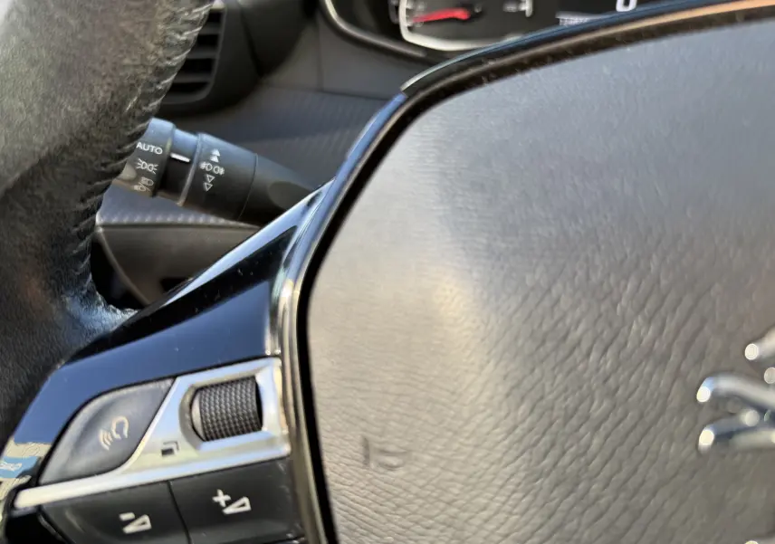 Gros plan sur le volant en cuir noir du Peugeot 2008 1.5 HDi 100 Active avec commandes intégrées et tableau de bord flou.