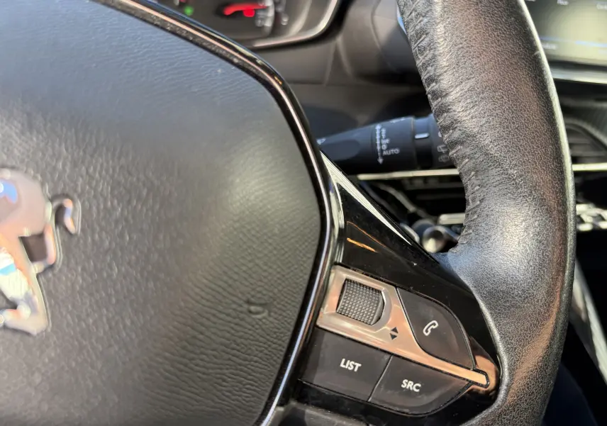 Gros plan sur le volant en cuir noir du Peugeot 2008 gris, avec commandes audio et téléphone intégrées.