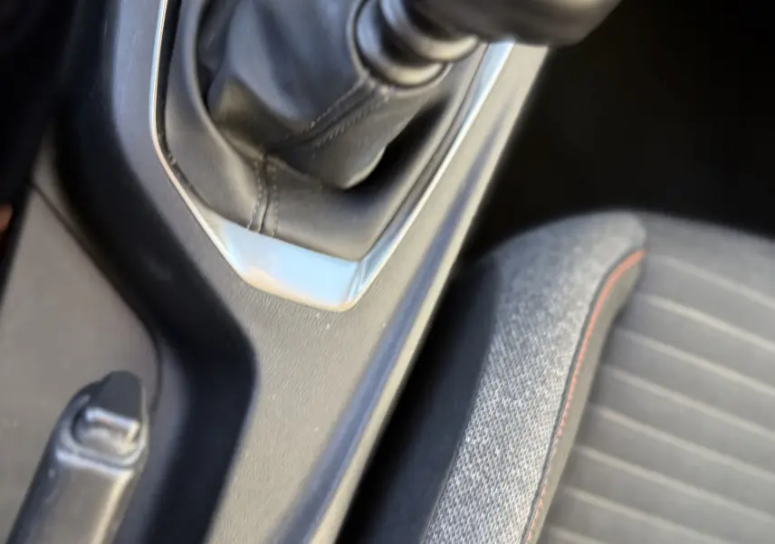 Gros plan sur le levier de vitesse manuel et la console centrale noire du Peugeot 2008 gris, avec siège tissu gris à couture orange.