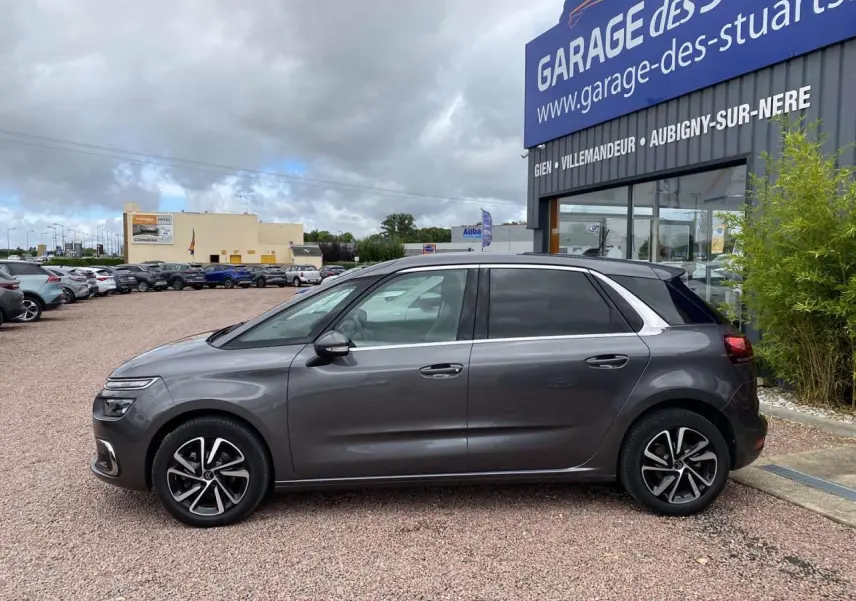 Profil côté gauche d'une Citroën C4 Spacetourer 2019 gris foncé, avec jantes alliage et vitres teintées, stationnée devant un garage.