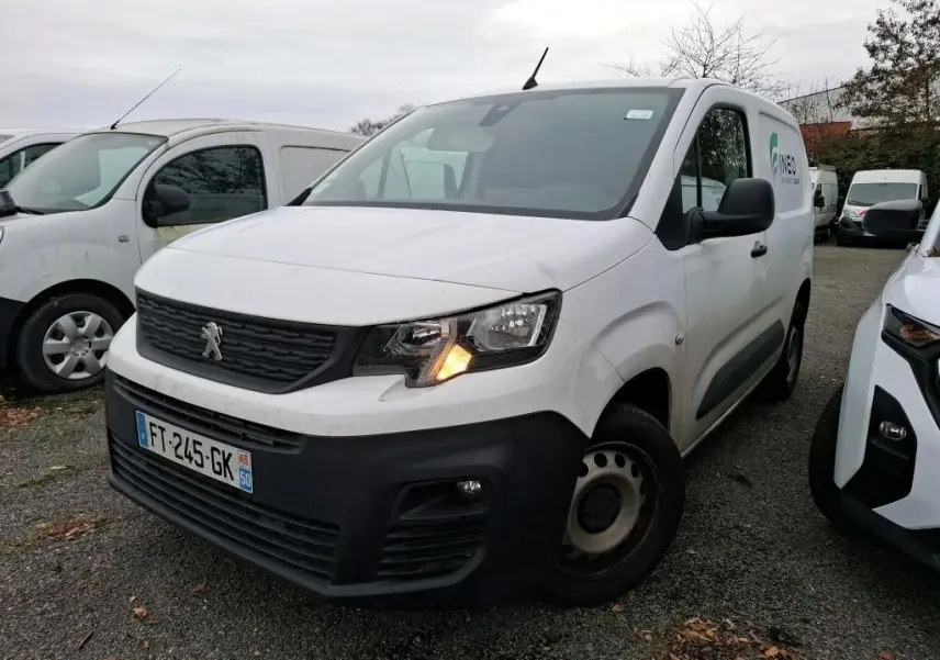 Fourgon Peugeot Partner blanc en 3/4 avant droit avec feu avant allumé sur parking extérieur.