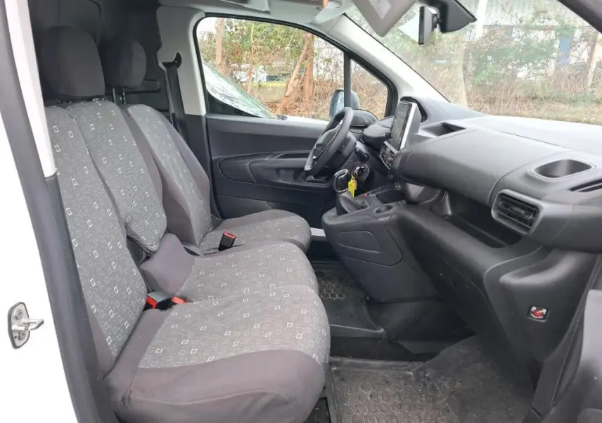 Vue intérieure côté conducteur du Peugeot Partner blanc 2020, montrant les sièges tissu gris et le tableau de bord noir.