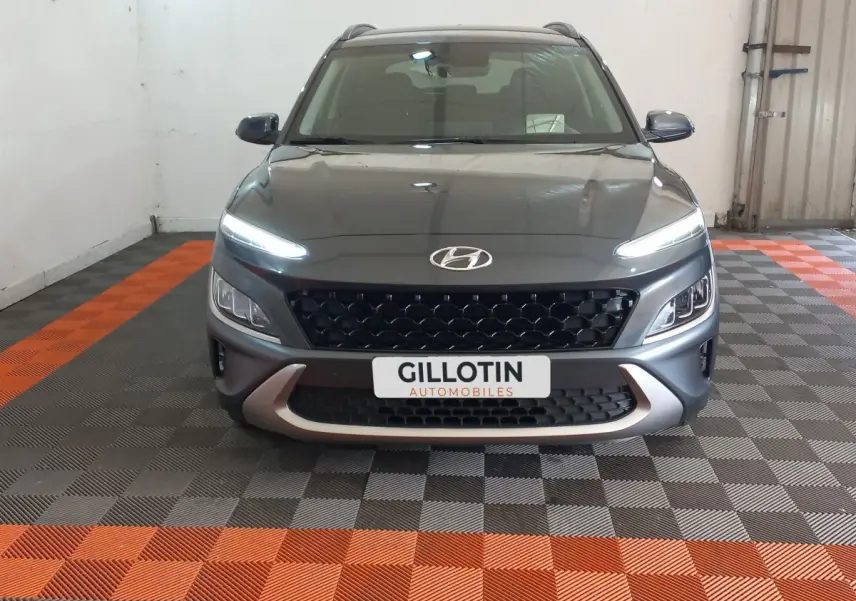 Vue avant d'un Hyundai Kona gris foncé avec feux LED allumés et calandre noire en intérieur showroom.