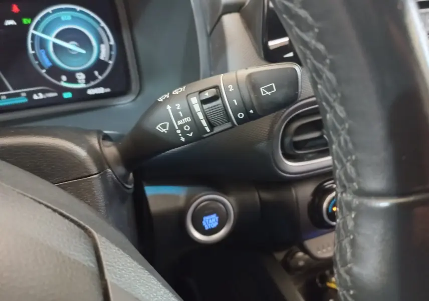 Gros plan sur la commande d’essuie-glace à gauche du volant cuir, avec tableau de bord numérique en arrière-plan.