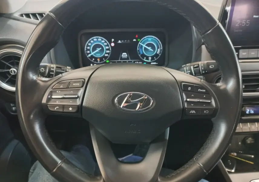 Vue rapprochée du volant cuir noir du Hyundai Kona 1.6 Hybrid 2022 avec commandes multifonctions et tableau de bord numérique.