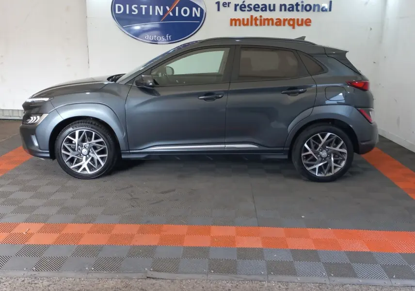 Vue latérale droite d'un Hyundai Kona gris foncé 2022, avec jantes alliage et toit noir contrasté en arrière-plan showroom.