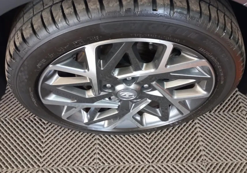 Gros plan sur la roue avant droite avec jante alliage gris et logo Hyundai visible sur un Hyundai Kona gris foncé.