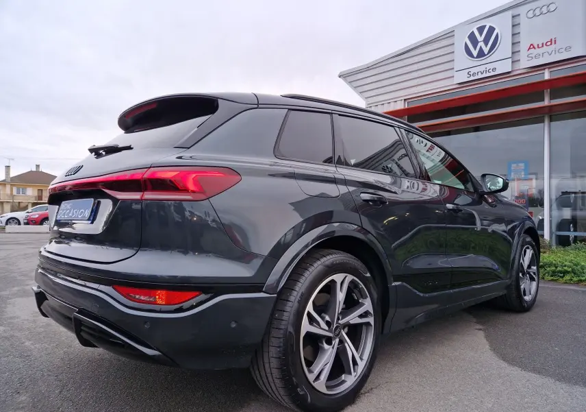 Audi Q6 e-tron Performance S-Line gris Manhattan, vue 3/4 arrière droit, feux arrière LED et jantes sport visibles.